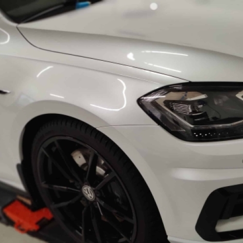 Polering af bil på hvid Volkswagen med fokus på glans og fjernelse af fine ridser.