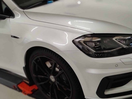 Polering af bil på hvid Volkswagen med fokus på glans og fjernelse af fine ridser.